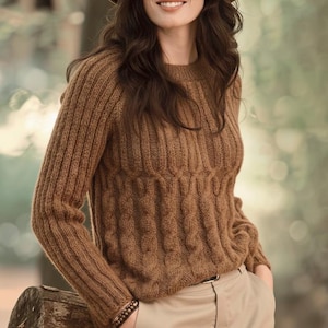 Puede incluir: Un suéter de punto marrón con un diseño acanalado en las mangas y un patrón de punto trenzado en el torso. El suéter tiene cuello redondo y mangas largas. La persona lleva un sombrero marrón y pantalones color caqui.