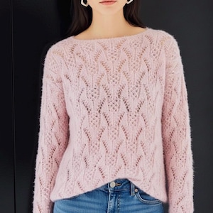 May include: A light pink, long-sleeved sweater with a delicate openwork design. The sweater has a boat neck and a slightly fuzzy texture. The sleeves are long, and the overall style is casual and feminine. The sweater is paired with blue jeans.