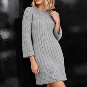 以下が含まれることがあります： 胴体と袖に縦リブ模様をあしらったライトグレーのニットワンピース。ラウンドネックと裾には複雑なケーブル編みのディテールが施されています。七分袖で、ストレートなシルエットの衣服です。