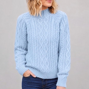 Può includere: Un maglione a trecce color azzurro con collo alto, maniche lunghe e polsini a coste. Il capo è realizzato con un motivo verticale testurizzato di trecce intrecciate e punti a maglia, che conferisce un aspetto coerente e uniforme.