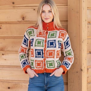 May include: A colorful, button-down cardigan with a geometric pattern. The sweater features squares in orange, green, blue, and cream, with an orange collar and cuffs. The model is wearing blue jeans.