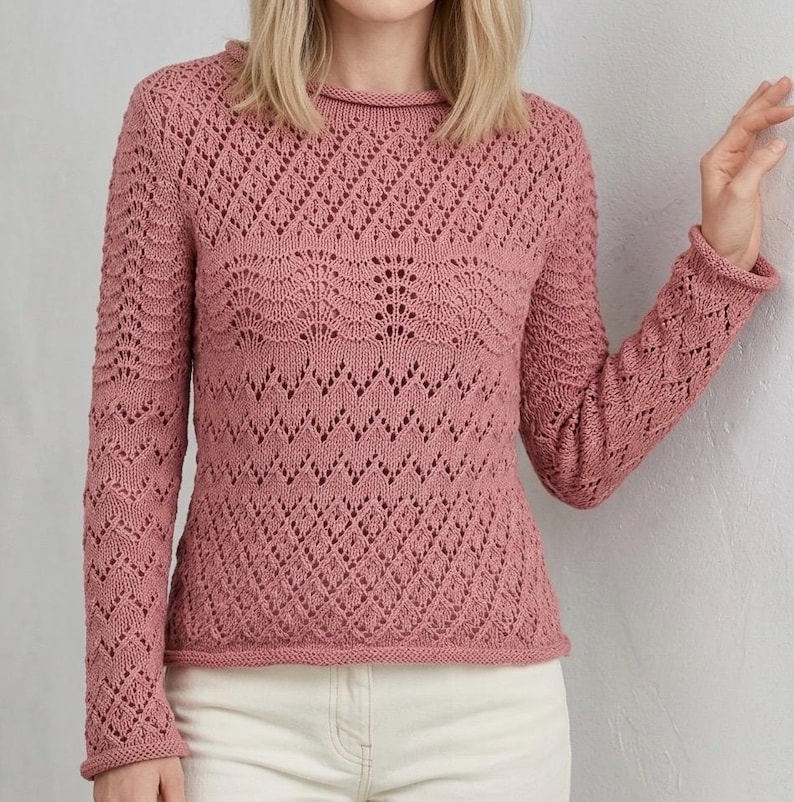 May include: A dusty rose knitted jumper with a round neckline and long sleeves. The jumper features a detailed openwork pattern across the chest and sleeves, with a ribbed hem and cuffs. The knitwear has a delicate, textured appearance.