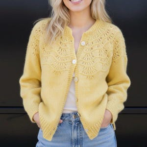 May include: A bright yellow knit cardigan featuring a round neckline, long sleeves, and a button-down front. The upper chest and shoulder area display an intricate, fan-shaped lace pattern, while the cuffs and hem are finished with ribbed knit detailing.
