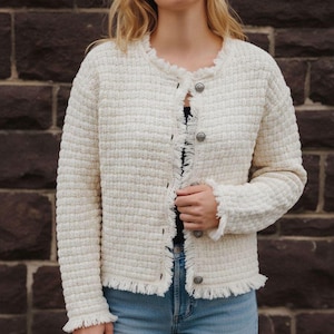 May include: Cream-colored textured jacket with a frayed trim around the collar, cuffs, and hem. The jacket has long sleeves and is fastened with three silver-toned buttons. The fabric has a woven appearance.