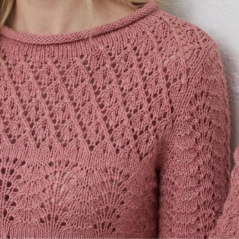 May include: A dusky pink knitted jumper with a crew neck and an intricate openwork diamond pattern. The sleeves are long, and the knit has a delicate, airy texture. The jumper is made of soft yarn, ideal for layering.