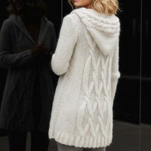 May include: A cream-coloured hooded cardigan with a cable knit design on the back. The long-sleeved sweater has a ribbed hem and cuffs. The model is wearing the sweater, and the back of the sweater is visible.