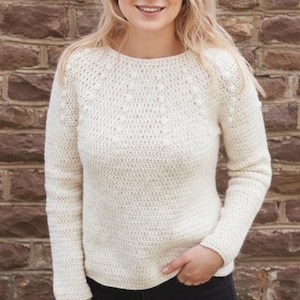 Peut inclure: Pull en crochet crème avec un col rond et des manches longues. Le pull présente un motif texturé de boules en relief sur la poitrine et le haut des manches. Le vêtement est fait d'un fil doux et texturé, idéal pour les temps frais.