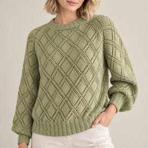 Può includere: Un maglione a maniche lunghe color verde salvia caratterizzato da un motivo a maglia traforata a forma di rombo sul davanti e sulle maniche. Il capo presenta uno scollo rotondo, polsini a coste e un orlo a coste per una vestibilità strutturata.