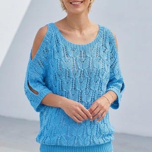 Puede incluir: Un suéter azul claro con hombros descubiertos, cuello redondo y mangas tres cuartos. La prenda de punto presenta un diseño calado texturizado. Las mangas tienen una abertura cerca del hombro. El suéter está hecho de un material suave y ligero.