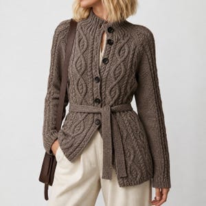 May include: A taupe cable-knit cardigan featuring a high collar, a front button closure with dark buttons, and a matching tie belt at the waist. The long-sleeved knit garment is worn over light-colored trousers and paired with a dark brown shoulder bag.