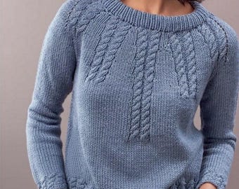 May include: A light blue knitted sweater with a round neckline and long sleeves. The sweater features a cable knit design on the front and along the shoulders, with ribbed cuffs and hem. The model is wearing the sweater with their hands in their pockets.