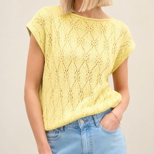 May include: A light yellow knit top with a diamond pattern. The short-sleeved shirt has a round neckline and is paired with light blue denim jeans. The top is made of a soft, breathable material.