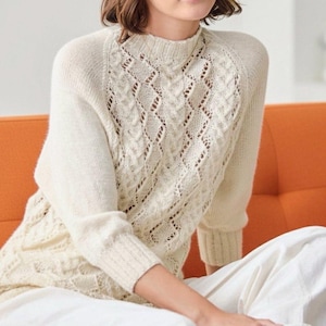 May include: A cream-coloured knitted jumper with a high neckline and a detailed diamond-shaped openwork pattern on the front. The long-sleeved jumper is made of a soft, textured yarn and has ribbed cuffs and hem.
