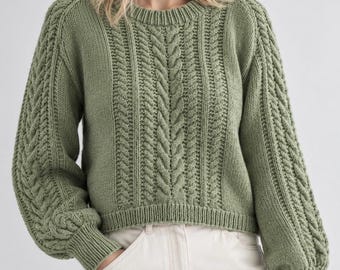 May include: A sage green long-sleeve sweater featuring a prominent vertical cable knit pattern on the front and sleeves, a round crew neckline, and ribbed cuffs and hem. The knit garment is paired with light-colored pants.