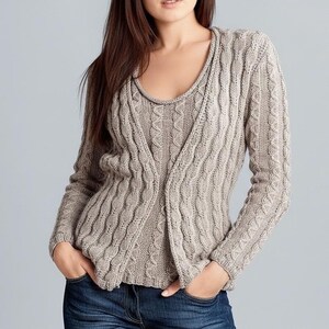 Pode incluir: Conjunto de camisola de malha entrançada castanha clara. O conjunto inclui um cardigan de manga comprida e um top de alças a condizer. O conjunto é feito de um material macio e texturizado e tem um design clássico. A modelo usa jeans azuis.