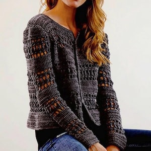 May include: A dark gray, open-weave crochet cardigan with long sleeves and a V-neck. The cardigan features a button-up front and intricate openwork patterns on the sleeves and body. The garment is made of a soft, textured yarn.