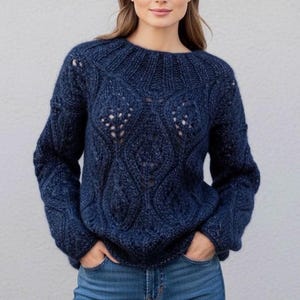 Könnte beinhalten: Ein marineblauer Strickpullover mit rundem Ausschnitt und langen Ärmeln. Der Pullover hat ein strukturiertes Lochmuster auf der Vorderseite und an den Ärmeln. Das Model trägt eine blaue Jeans.