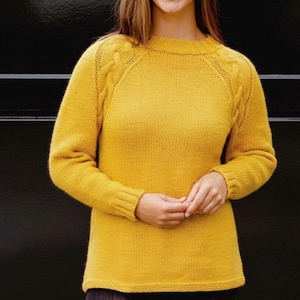May include: A mustard yellow sweater with a crew neck and long sleeves. The sweater features cable knit detailing on the shoulders and cuffs. The knitted garment is made of a soft, textured material.