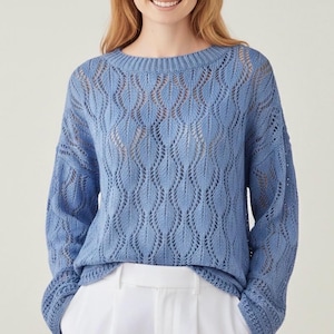 May include: A pale blue knitted jumper featuring an openwork leaf design. The jumper has a round neckline and long sleeves with ribbed cuffs. The hem is also ribbed. The jumper is worn with white trousers.