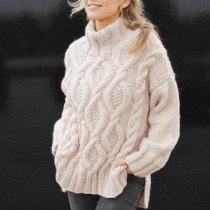 Może przedstawiać: Kremowy sweter z warkoczowym splotem i golfem. Sweter ma wzorzysty wzór ze splecionych kabli i rozcięcie u dołu. Rękawy są długie, a styl jest obszerny i wygodny.