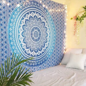 May include: A blue and white mandala tapestry hanging on a wall above a bed. The tapestry features a large, detailed circular design with a gradient effect. Fairy lights and decorative plants add to the room's ambiance.