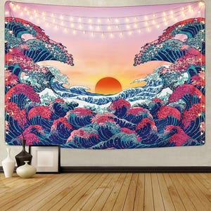 Puede incluir: Un tapiz con una escena de puesta de sol vibrante con olas oceánicas estilizadas en tonos azules, rosas y blancos. El sol es un gran círculo naranja. Una guirnalda de luces cuelga en la parte superior. Arte mural decorativo.