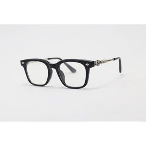 May include: Black square-framed spectacles with clear lenses. The frames feature a decorative silver accent on the temples and small diamond-shaped details on the front. The glasses are set against a white background.
