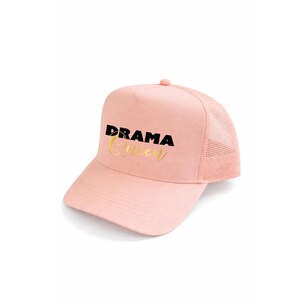 Peut inclure: Casquette de camionneur rose avec un dos en filet et une visière incurvée. Le chapeau porte l'inscription "DRAMA Queen" en lettres noires et dorées sur le devant. Fermeture à pression réglable.