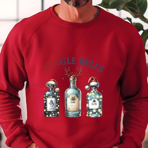Könnte beinhalten: Roter Pullover mit festlichem Weihnachtsdesign. Er zeigt drei Gin-Flaschen, die mit Weihnachtsmützen, Lichterketten und Rentiergeweihen geschmückt sind. Auf den Flaschen steht das Wort "GIN", und der Text "Jingle Bells" ist sichtbar.
