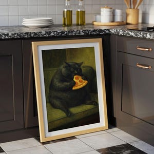 May include: A framed print featuring a black cat eating a slice of pizza. The cat is depicted sitting on a green couch. The artwork has a light wood frame and is displayed on a kitchen counter.