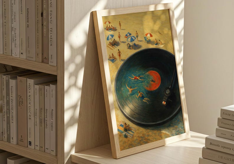 May include: Framed art print featuring a beach scene with people swimming in a vinyl record. The artwork has a light wooden frame and is displayed on a wooden surface next to a bookshelf and a stack of books.