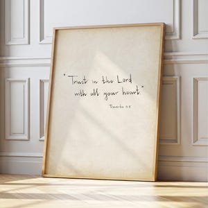 Può includere: Una stampa incorniciata con la citazione "Trust in the Lord with all your heart" in scrittura nera. La stampa ha un aspetto di carta vintage ed è incorniciata in una cornice di legno chiaro. Il testo "Proverbi 3:5" è sotto.