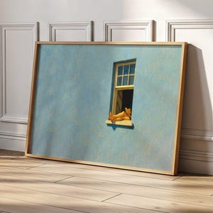Puede incluir: Una obra de arte enmarcada representa una pared azul con una ventana amarilla. La ventana está abierta y se ven las piernas de una persona, descansando en el alféizar. La obra está enmarcada en madera clara y se apoya en una pared.