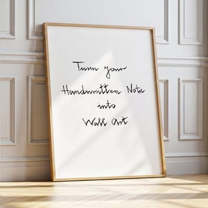 Peut inclure: Une impression encadrée blanche avec le texte "Turn your Handwritten Note into Wall art" en écriture noire. Le cadre est de couleur bois clair, et l'impression est appuyée contre un mur blanc et un sol en bois.