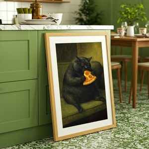 May include: A framed art print depicts a black cat seated on a green sofa, eating a slice of pizza. The artwork is in a light wood frame, leaning against a green kitchen cabinet. The kitchen has a white countertop and a patterned green and white floor.