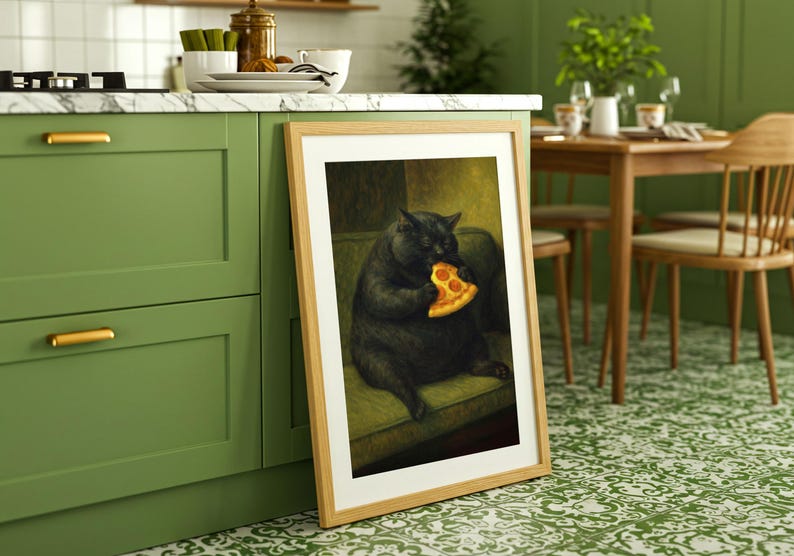 May include: A framed art print depicts a black cat seated on a green sofa, eating a slice of pizza. The artwork is in a light wood frame, leaning against a green kitchen cabinet. The kitchen has a white countertop and a patterned green and white floor.