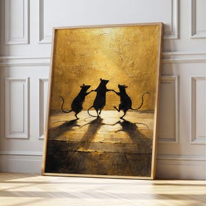 Puede incluir: Una impresión artística enmarcada que presenta tres siluetas negras de ratas bailando sobre un fondo dorado texturizado. La obra de arte, con sus tonos cálidos, se exhibe sobre un suelo de madera. El marco es de madera clara.