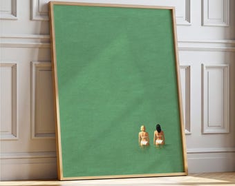 May include: A framed art print featuring two figures in white swimwear standing in green water. The artwork has a minimalist style with a solid green background and a light brown frame.