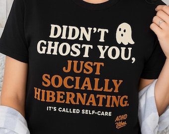 May include: Black t-shirt with the text "DIDN'T GHOST YOU, JUST SOCIALLY HIBERNATING. IT'S CALLED SELF-CARE" in white and orange lettering. A small ghost graphic is on the right. The shirt has the words "ADHD Vibes" at the bottom.