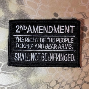 May include: Black rectangular patch with white embroidered text. The text reads "2ND AMENDMENT" above "THE RIGHT OF THE PEOPLE TO KEEP AND BEAR ARMS, SHALL NOT BE INFRINGED."