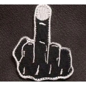 May include: An embroidered patch featuring a black hand silhouette with a raised middle finger. The design is outlined in white thread, with white stitching detailing the fingernail and finger joints against a solid black background.