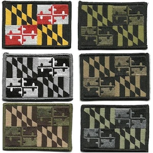 May include: A collection of embroidered patches featuring the Maryland state flag design. The patches display the flag's distinctive black and gold, red and white, and black and white patterns, along with other color variations. Each patch is rectangular with a black border.