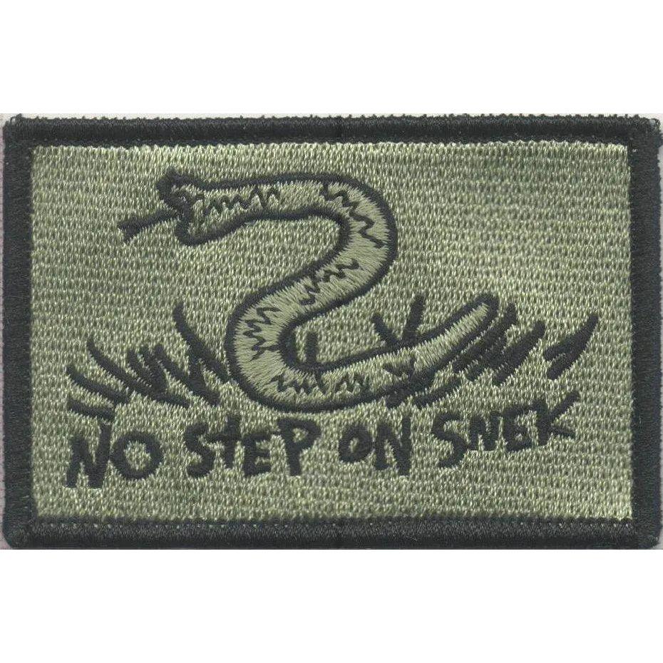Pode incluir: Um emblema retangular bordado em verde-oliva com uma borda preta. O emblema apresenta uma ilustração bordada em preto de uma cobra na grama e o texto NO STEP ON SNEK em uma fonte de estilo manuscrito centralizado na parte inferior.
