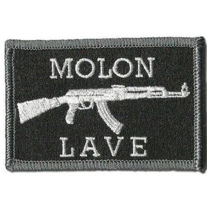 Pode incluir: Um emblema retangular preto bordado com uma borda cinza. O emblema apresenta o texto branco bordado MOLON acima de um gráfico de rifle branco e o texto LAVE abaixo do rifle. O design está centralizado em um fundo de tecido preto.