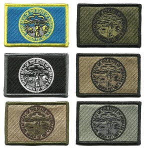 May include: Rectangular embroidered patches featuring the Nebraska state seal. The patches come in various colors, including blue, black, olive green, tan, and gray. Each patch displays the state seal with the text "GREAT SEAL OF THE STATE OF NEBRASKA MARCH 1ST 1867".