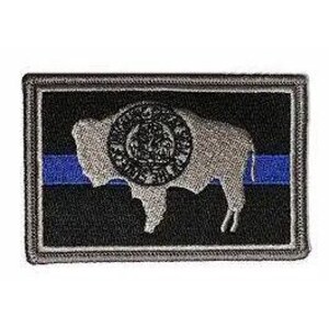 May include: A rectangular embroidered patch featuring a black background with a horizontal blue stripe across the center. A silver-toned silhouette of a buffalo is centered on the patch, overlaid with a circular emblem containing detailed imagery.