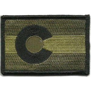 May include: A rectangular embroidered patch featuring a muted olive green and black colour scheme. The design displays a horizontal stripe pattern with a large, circular black letter C emblem positioned on the left side of the patch.