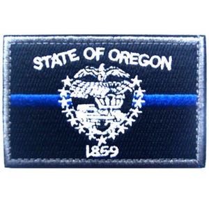 Peut inclure: Un écusson rectangulaire brodé noir avec le texte blanc STATE OF OREGON au-dessus d'un emblème d'aigle blanc entouré d'étoiles, avec l'année 1859 en dessous. Une fine ligne bleue horizontale traverse le centre de l'écusson.