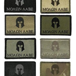 May include: Rectangular patches in various colors, including black, olive green, and camouflage, each featuring a Spartan helmet emblem and the Greek phrase "MOLON LABE" in white or gray. The patches are likely for tactical gear or apparel.