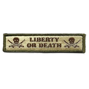 May include: A rectangular embroidered patch with an olive green border and a tan background. The text LIBERTY OR DEATH is centered in brown lettering, flanked by two brown skull icons, each positioned above two crossed rifles in brown thread.